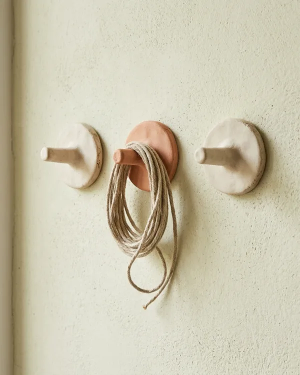 Three clay wall hooks with short pegs, one holding coiled linen cord