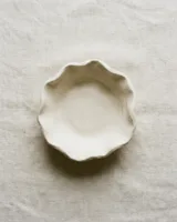 Shallow off-white air dry clay bowl with a softly wavy rim on pale linen