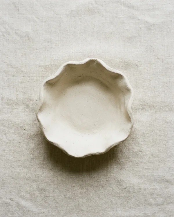 Shallow off-white air dry clay bowl with a softly wavy rim on pale linen