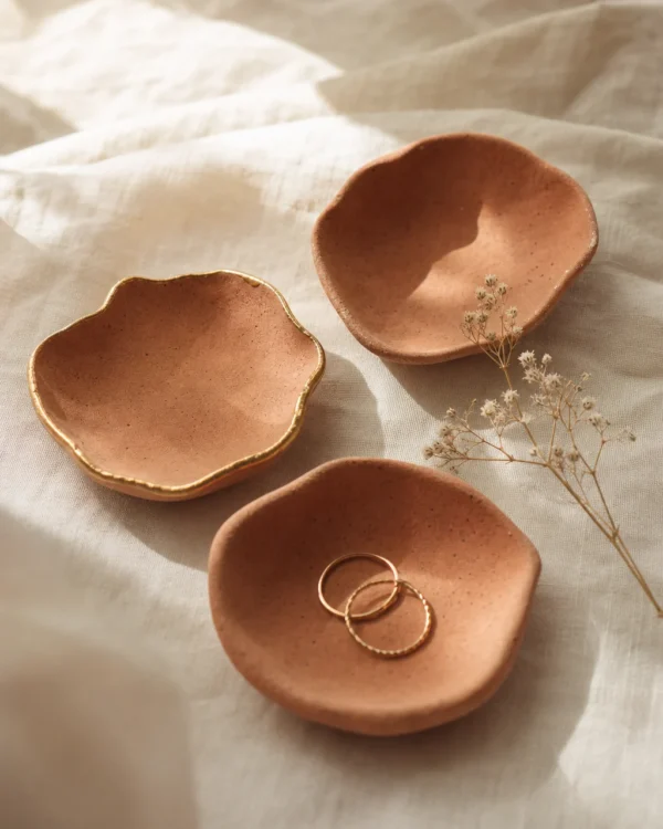 Three terracotta clay trinket dishes with organic edges, one holding gold rings