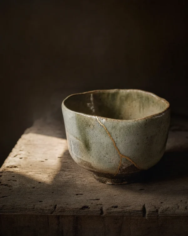 A wabi sabi tea bowl with an uneven rim and a gold kintsugi repair seam