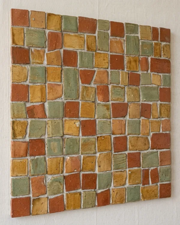 A hand-cut clay tile accent wall glazed in terracotta, ochre and sage